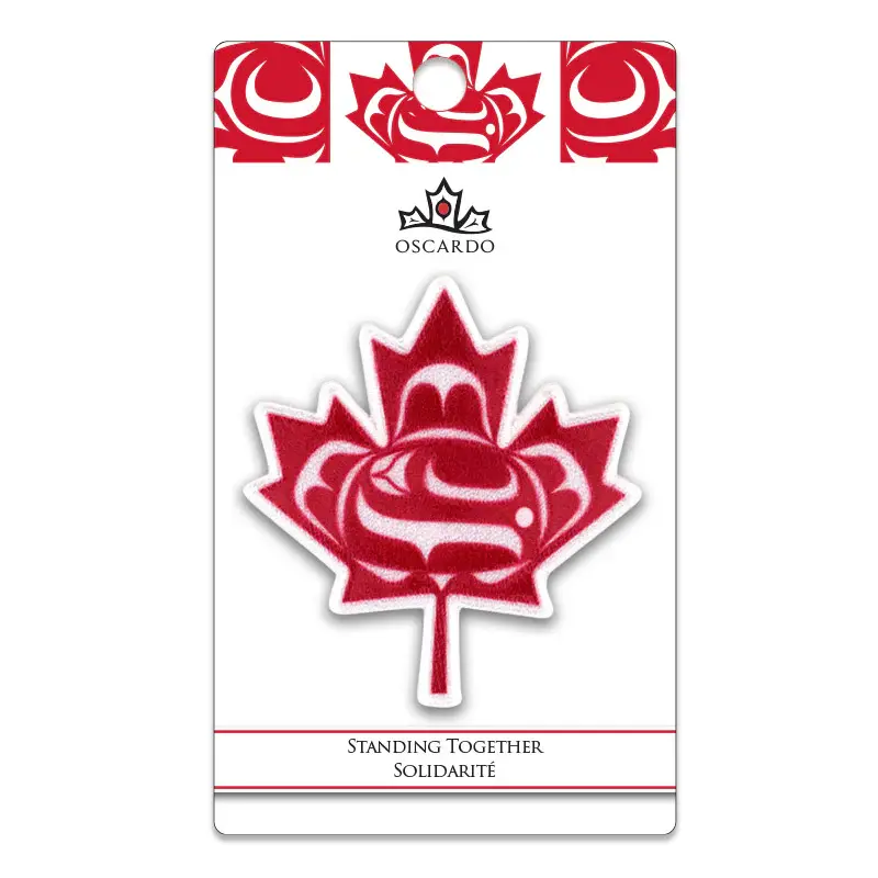 Packaged iron-on patch in shape of maple leaf with red & white reproduction of artist Curtis Wilson's 'Standing Together'