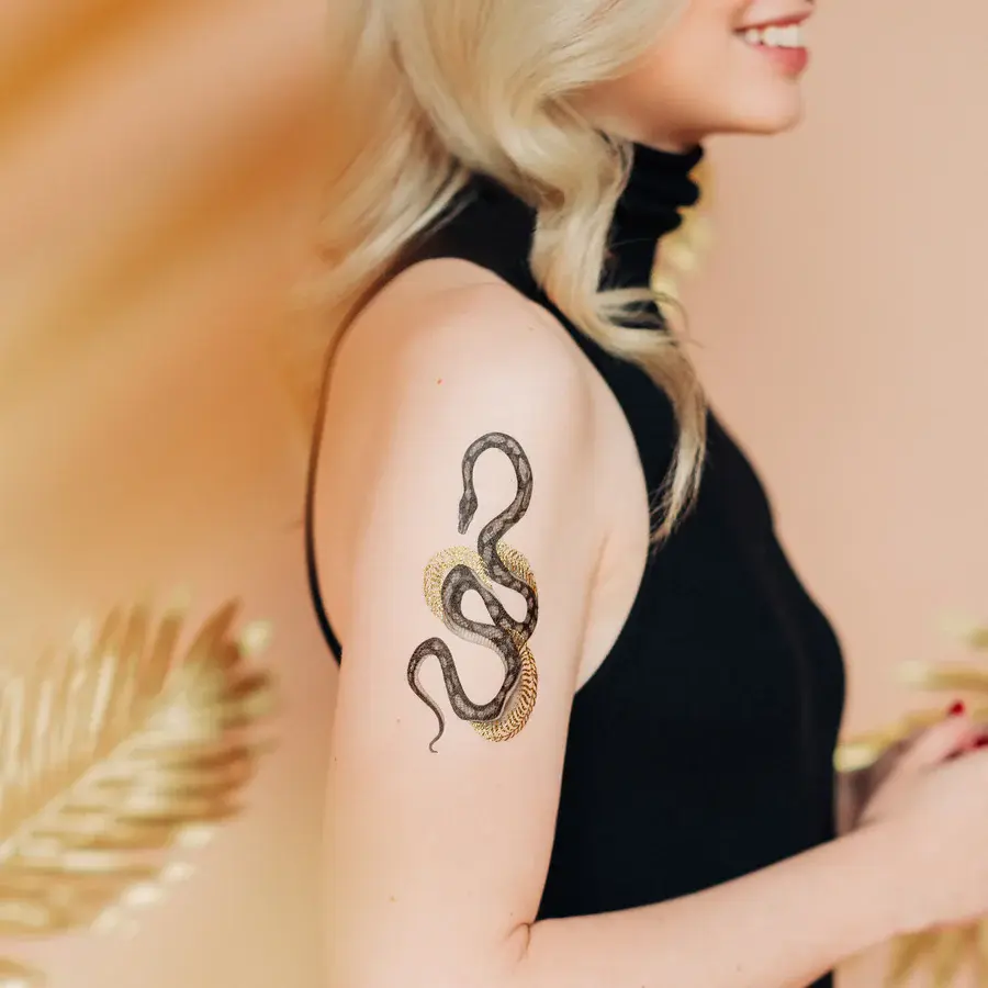 Thumbnail: Side view of blond model in black dress with tattoo of black & gray snake shedding golden skin on upper arm