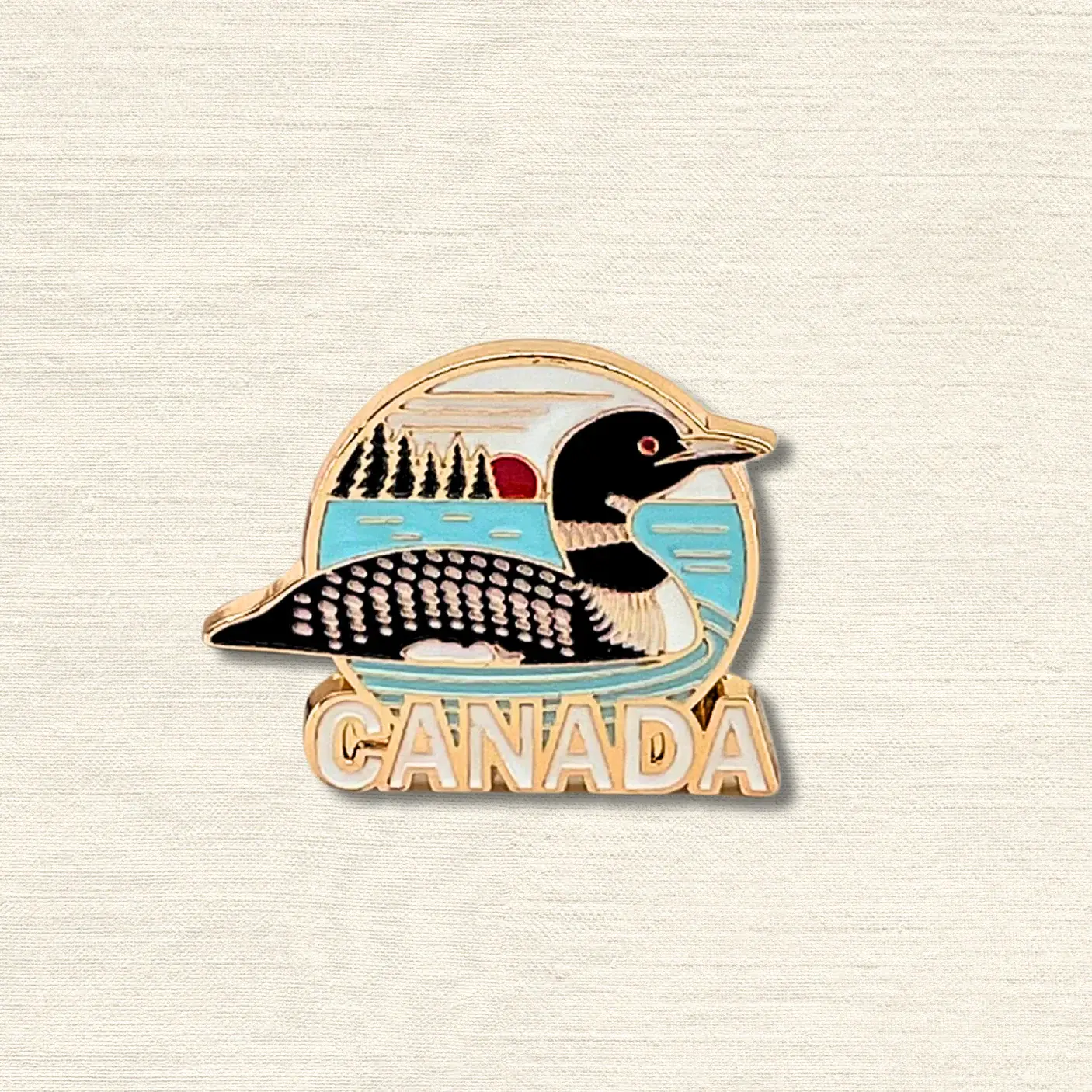 Gold, black, white, & blue enamel pin in shape of loon with text, 'Canada'