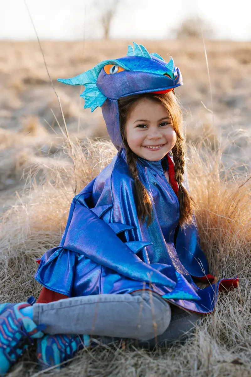 Front view of seated child wearing shiny blue metallic dragon cape with fierce eyes, horns & spiked tail