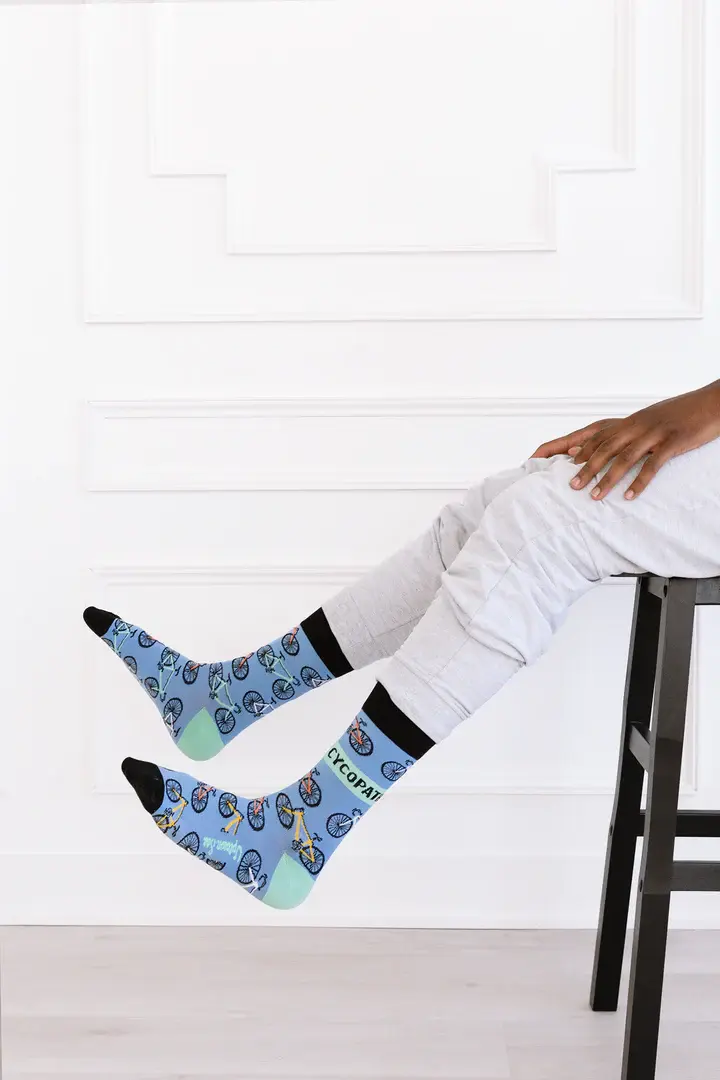Seated model wearing blue & navy socks with bicycle print, text on side, 'Cycopath'