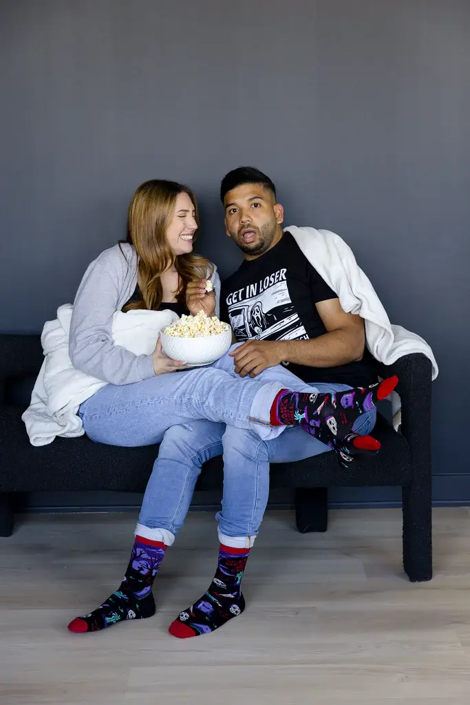 Couple cuddled on couch with popcorn wearing Stream & Scream socks