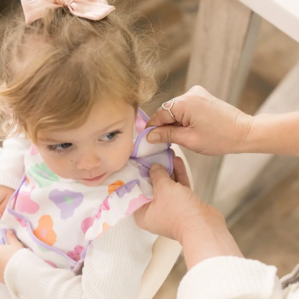 A close-up of a parent adjusting the gentle, scratch-free shoulder closure on a Tiny Twinkle bib at Tickled Pink.