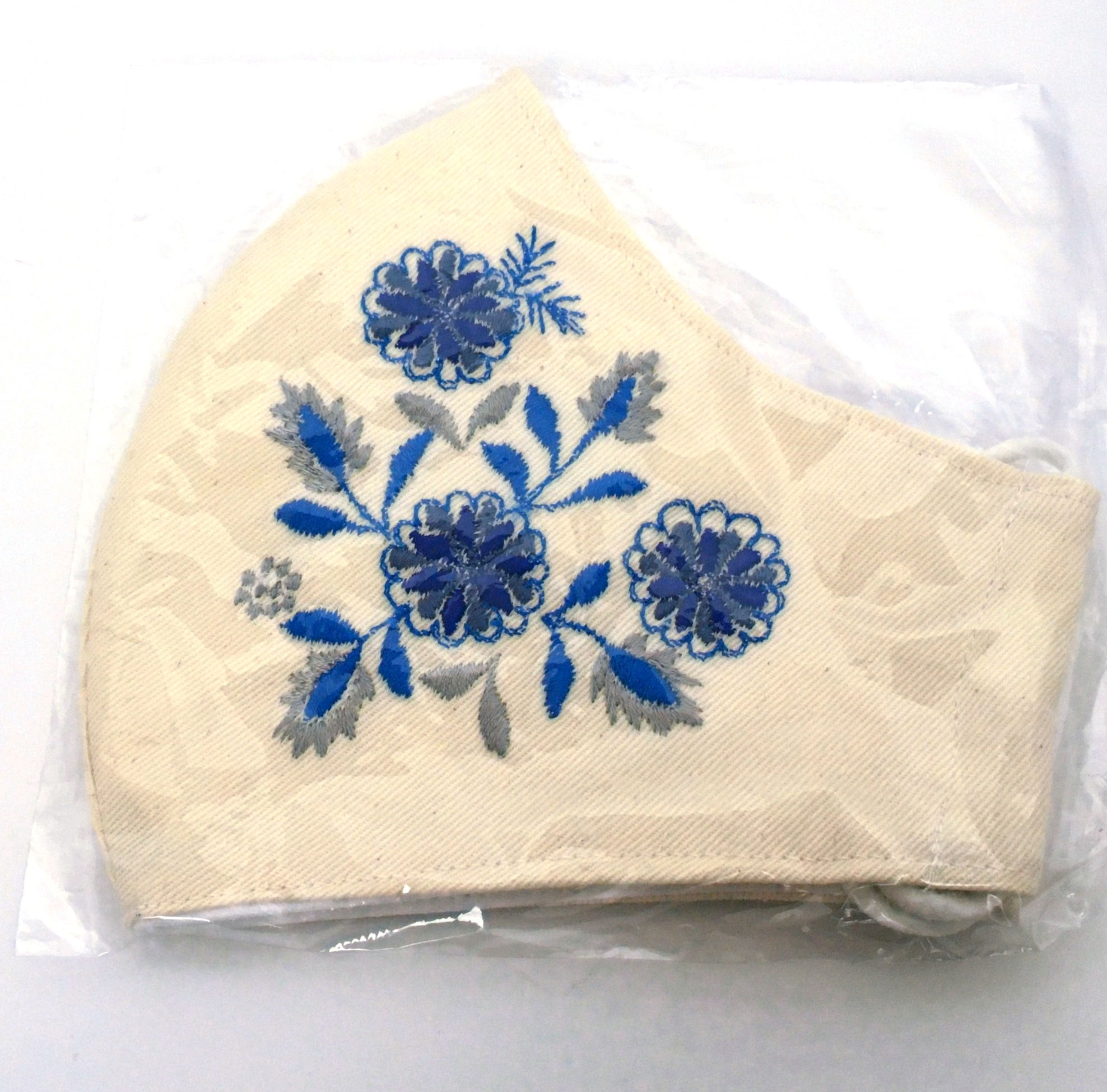 Side view of folded cream embroidered mask with bright blue, indigo & silver gray floral pattern