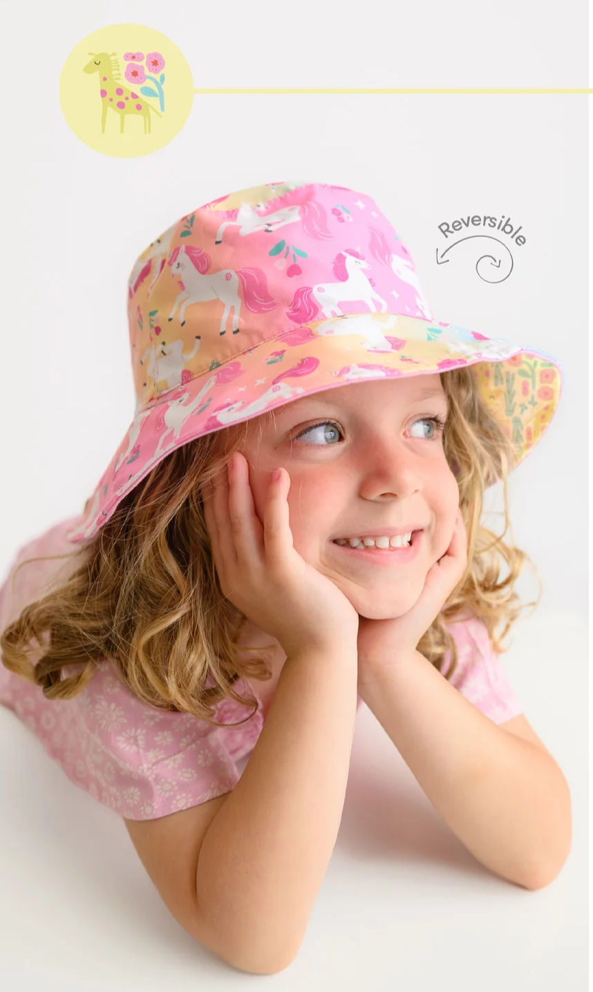 A smiling model wearing the reversible unicorn and giraffe hat at Tickled Pink.