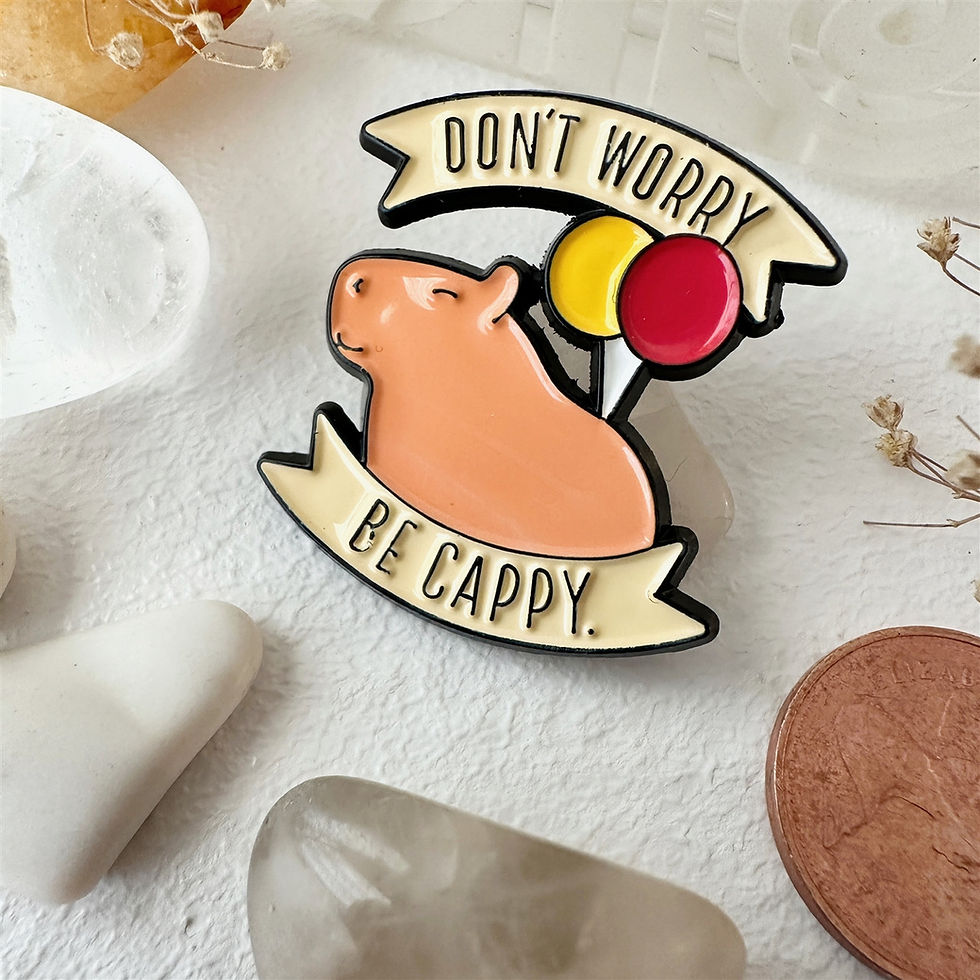 Lapel pin of pink capybara & red & yellow balloons with text, 'Don't worry, be cappy.'