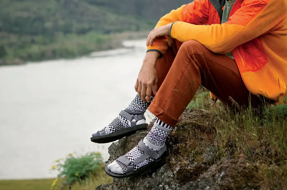 Seated model wearing mismatched crew socks in black, white & grays with knit pattern