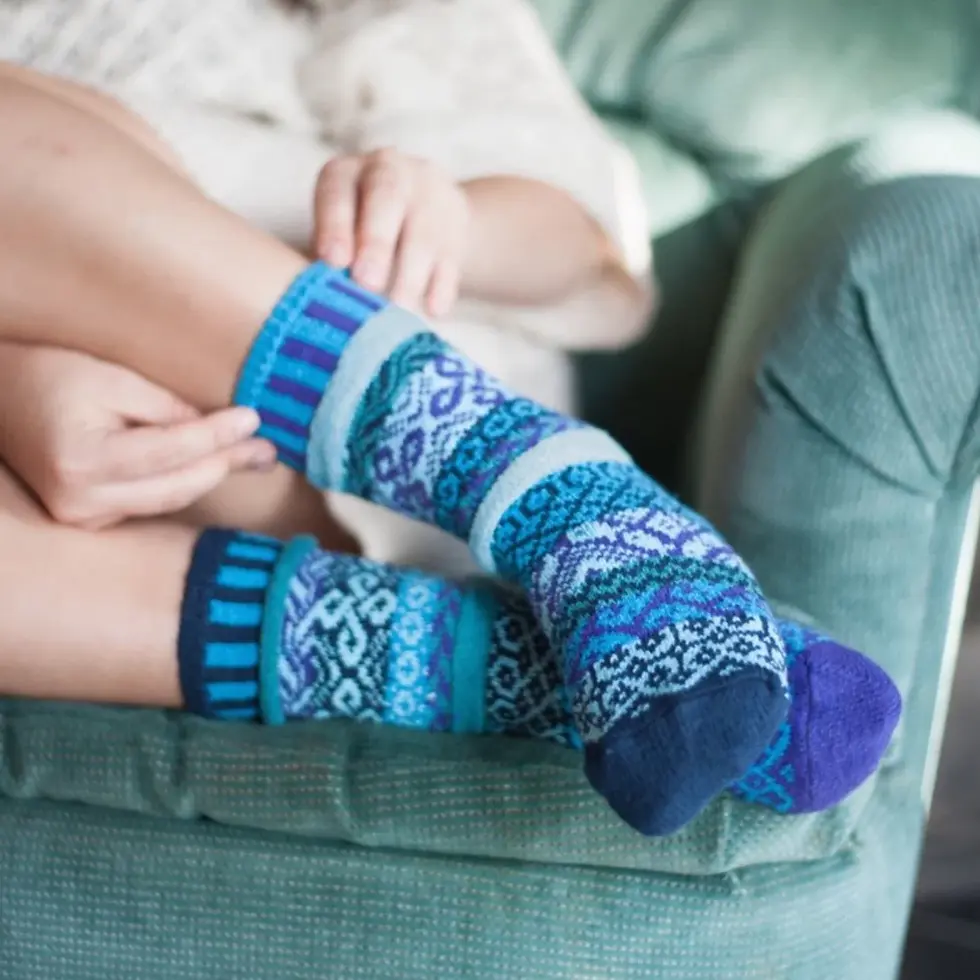 Reclining model wearing mismatched knit crew socks in turquoise, purple, jade, navy & teal.
