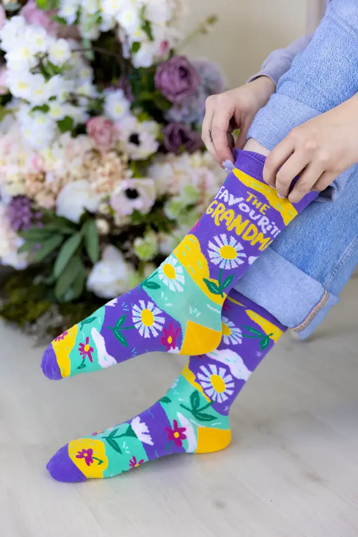 Model wearing purple, green & yellow socks with daisy print, text on side, 'The Favourite Grandma'