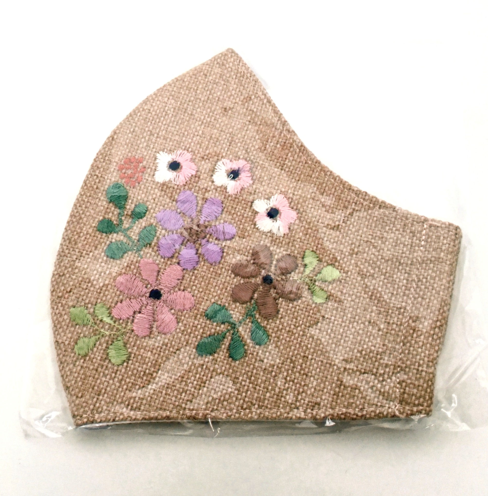 Side view of folded embroidered fawn cotton mask with flowers in pinks, lilac & bronze & 2 tone green leaves
