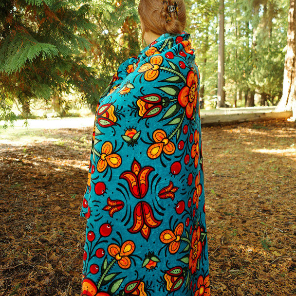 Model in forest wrapped in rectangular fleece blanket with print of artist Justine Proulx's 'Prairie Beadwork'
