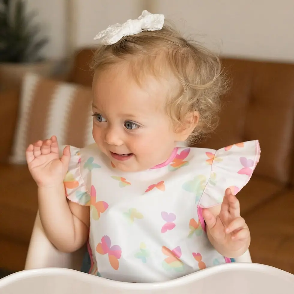 A baby in a high chair wearing a ruffled butterfly pattern Tiny Twinkle easy bib at Tickled Pink.