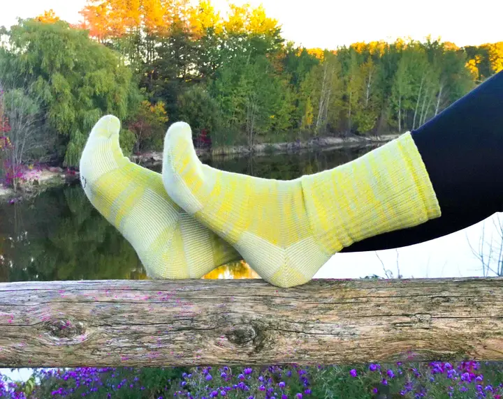 Model's feet on log by lake wearing yellow socks with lighter heel & toe