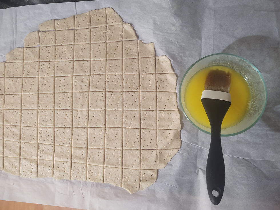 Dough with perforated squares on parchment paper beside a bowl of melted butter, with a brush ready for application.