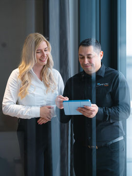 Zwei lächelnde Kollegen betrachten gemeinsam ein Tablet im modernen Büro.