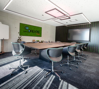 Moderner Konferenzraum, SONEXTIS Logo an grüner Mooswand, mit großem Bildschirm.