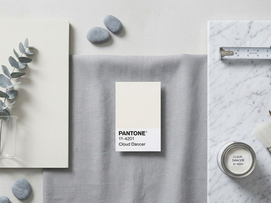Pantone Cloud Dancer paint swatch styled with marble, paint brushes, soft grey fabric, and natural decor elements