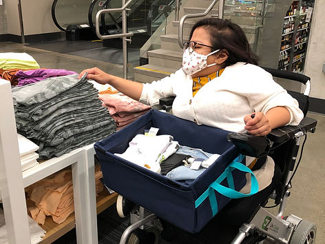 A young woman wheelchair user with dark hair uses her LapSnap adaptive carryall to shop for clothing and other items.