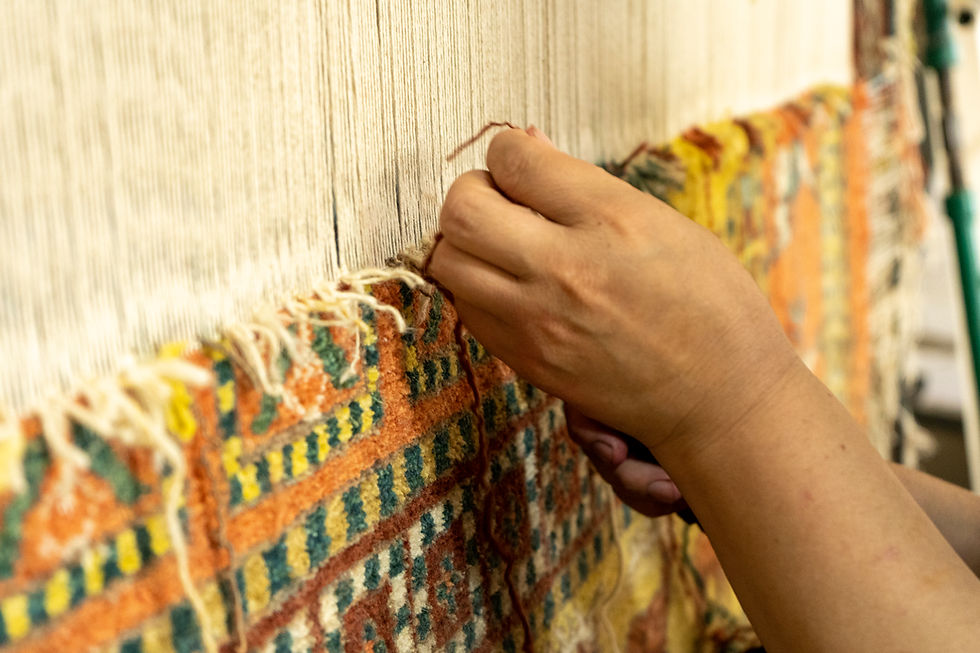Hands weaving a colorful patterned rug on a loom, close-up, with soft workshop lighting.