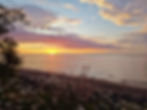 Sunset over a calm beach and lake, with wildflowers in the foreground and pastel clouds glowing over Lake Superior.