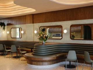 Interior of Chit Chat Coffee in Los Angeles featuring several Naaya Poppy ceramic wall sconces mounted on a light-colored wall above a wooden bench seating area. The space is bright with modern furniture and large glass windows.