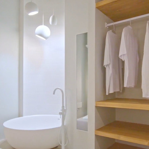 Minimalist white bathroom with a round freestanding tub and a trio of white globe ceramic pendant lights hanging at varying heights near open shelving.