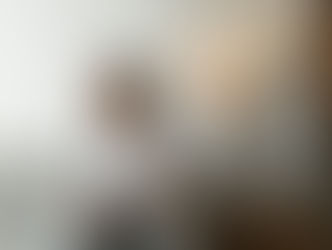 A woman with brown hair sits on a grey couch, smiling and talking. To her right, three modern, organic-shaped ceramic pendant lights (the Naaya Drops) hang, glowing warmly.