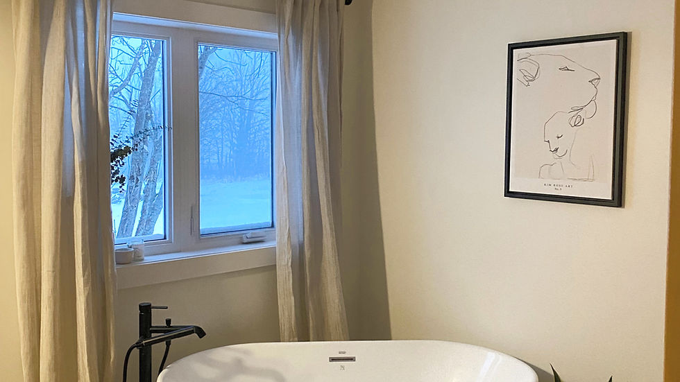 Cozy bathroom corner with a white freestanding soaking tub, natural linen curtains, and a minimalist beige ceramic flush mount ceiling light.