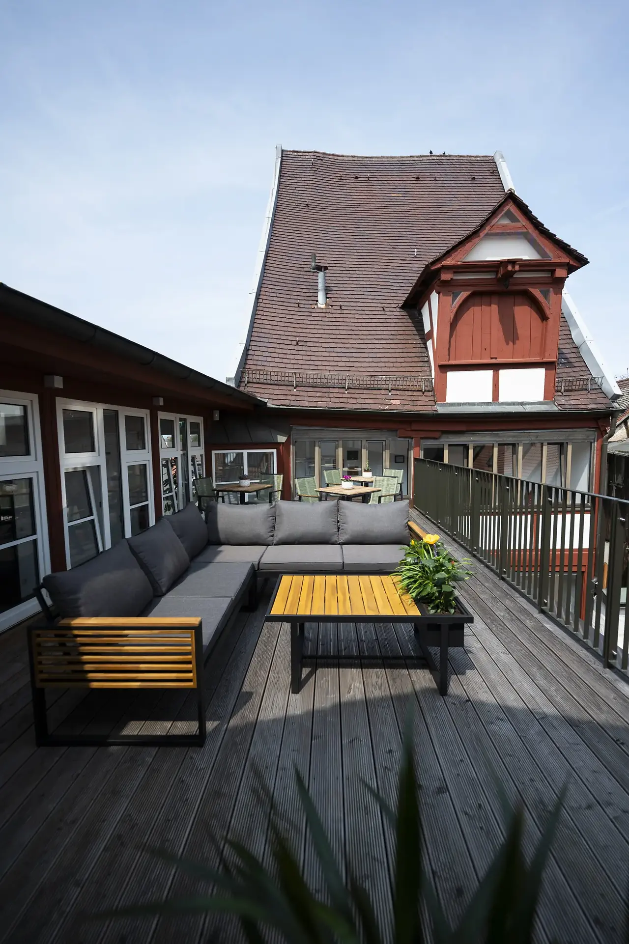 Outdoor rooftop patio terrace at Hotel Sandkorn featuring dark grey lounge seating, wooden coffee tables, and traditional German timber-framed architecture in the background.