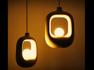 A collection of sculptural ceramic pendant lights by Naaya Studio in organic, perforated, and asymmetrical shapes, glowing warmly in a softly lit room.