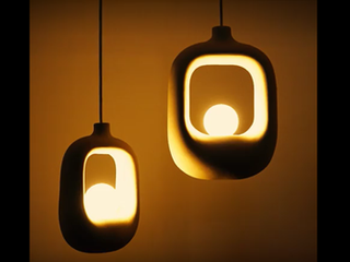 A collection of sculptural ceramic pendant lights by Naaya Studio in organic, perforated, and asymmetrical shapes, glowing warmly in a softly lit room.