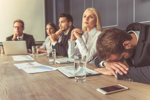 Group of people in corporate office. One man is lying with head on the desk.