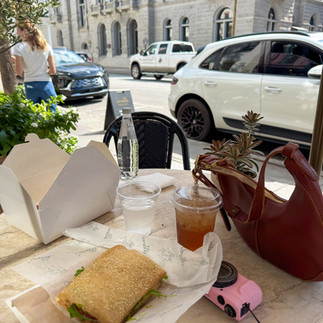 a lunch set up with a sandwich, iced tea, brown leather purse set against a city backdrop