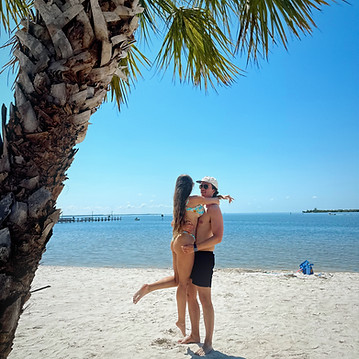 Jules Anderson and her fiancé dancing on the beach with blue skies and a palm tree