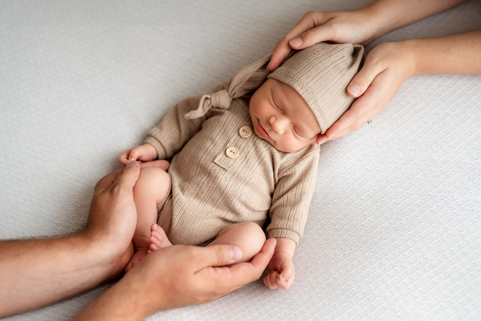 Spící miminko se sleepy čepičkou a v nádherném beige overálku v rukách rodičů, během newborn focení v ateliéru ve Frýdlantu nad Ostravicí. Certifikovaná fotografka miminek. Foceni miminek, rodinné focení s miminkem, newborn focení ostrava, foceni miminek doma.