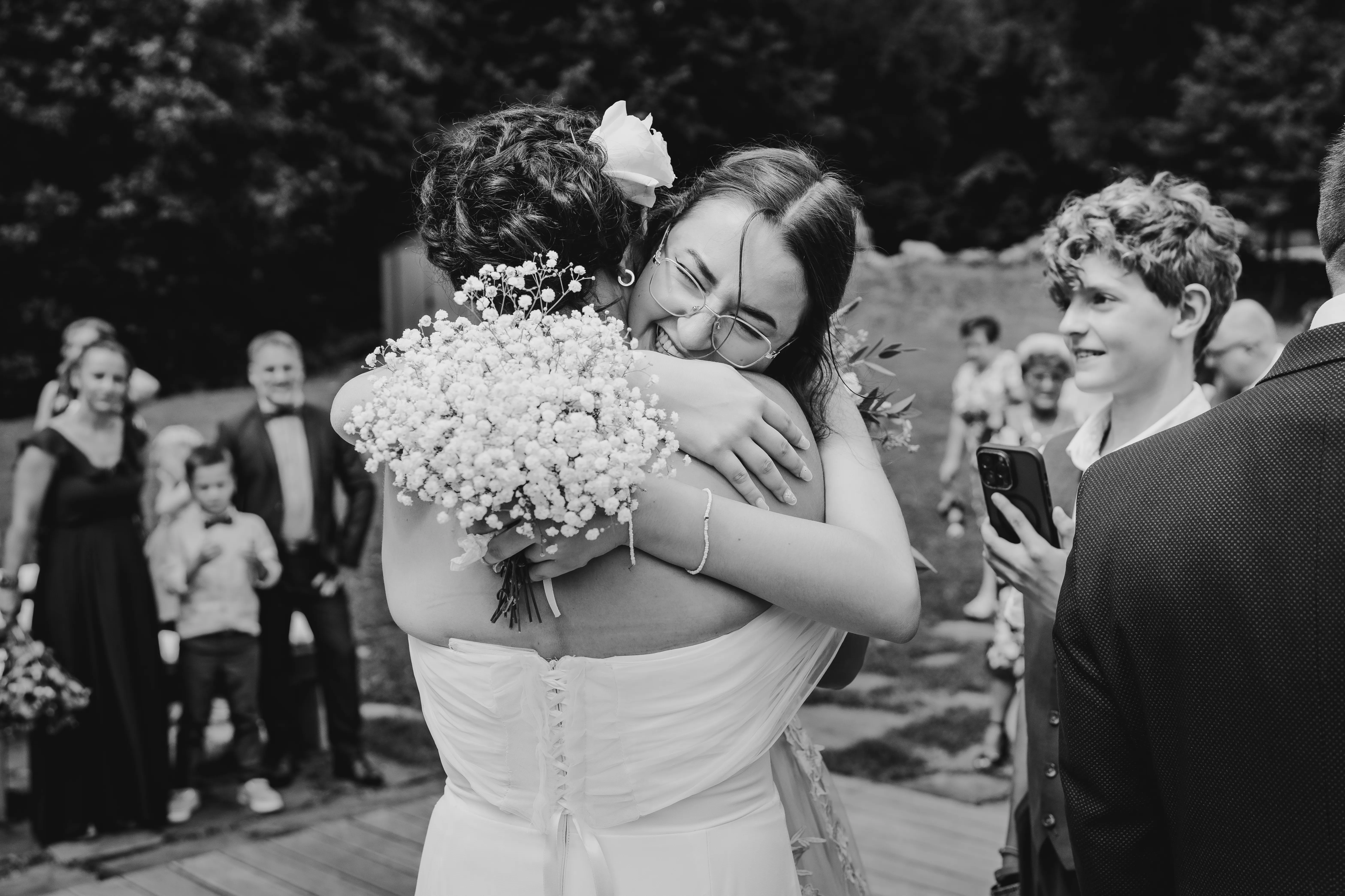 Emotivní černobílá fotografie zachycující okamžik gratulací novomanželům, plná upřímných emocí a radosti. Tento moment zachycuje hluboké lidské spojení a štěstí, které vyzařuje z každého úsměvu. Svatební fotograf Ostrava, Moravskoslezský kraj. Svatební fotky s důrazem na emoce. Svatební fotografka.