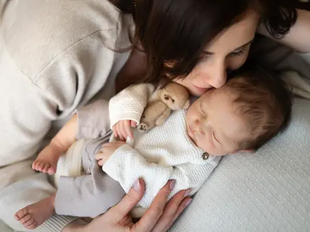 Lifestyle newborn focení s maminkou zachytilo spící miminko v jemných neutrálních barvách, držící malého medvídka.