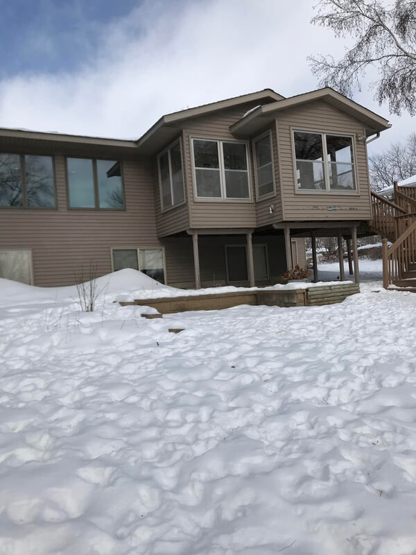 Lake side view of home with sun room on posts, brown siding.
