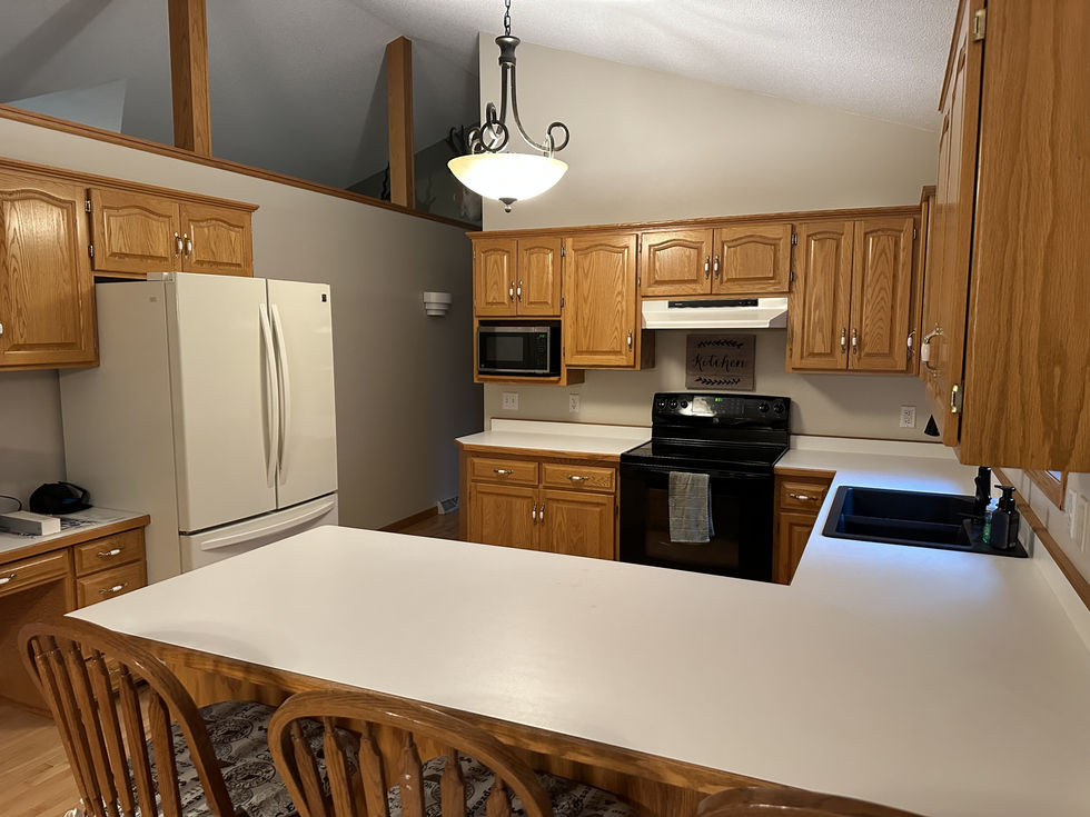 Natural stained oak cabinetry, off white Formica countertops, white refrigerator, black stove.