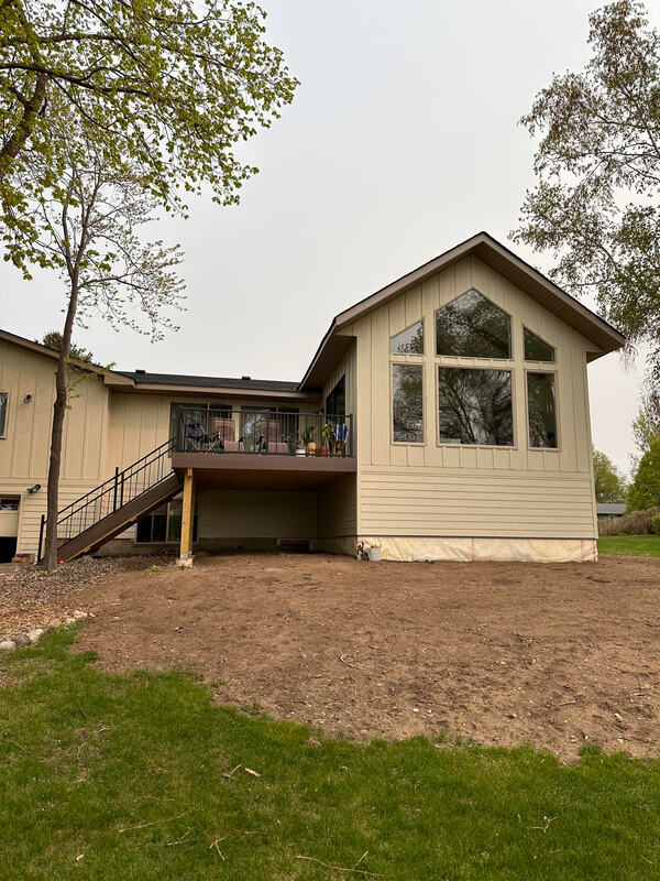 Exterior view of lakeside great room with wall of windows, tana siding, and brown roof.