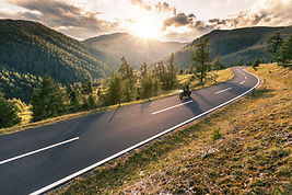 A wide shot of a person riding a motorcycle against a bright sunset.