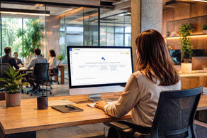 Mulher de costas usa computador em escritório moderno; na tela, interface Neo Office, com sala de reunião e plantas ao fundo.