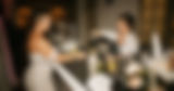Two bartenders smiling behind a mobile bar setup, one pouring a cocktail as the other preps glassware during a lively event.