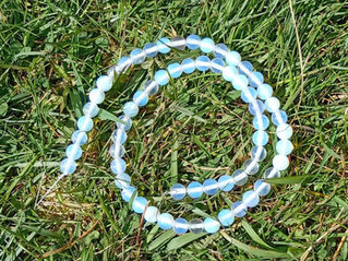A string of opalite beads lie on green grass.