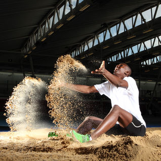 Team GB Olympic long jumper Jermaine Olasan in a white shirt and green shoes is throwing sand in the air