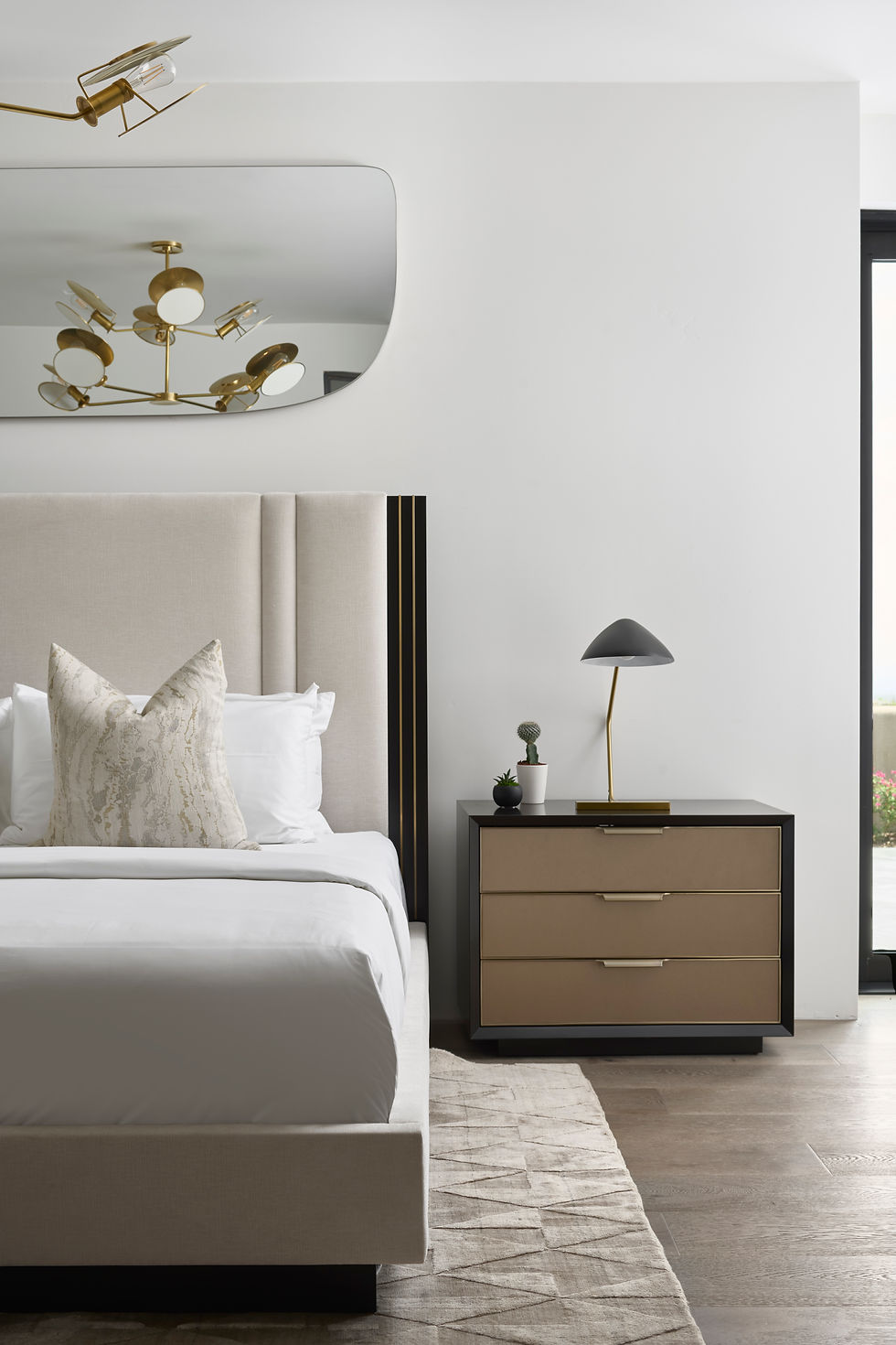 Timeless modern bedroom. clean lines with neutral colors. Brass nightstand with brass table side light. Soft headboard with accent pillows. Brass chandelier with soft sculptural details . Viscose rug in a neutral tone. Wide plank wood flooring.