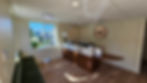 A peaceful room with a massage table, potted plant, cabinet, and spine chart on a pale blue wall. Warm, calm atmosphere.