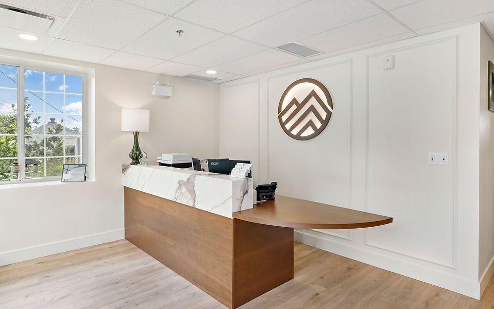 Saanichton Chiropractic Group bright empty office reception with marble-and-wood desk, lamp, window, and glowing circular wall logo; Acer monitor visible.