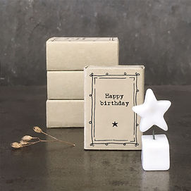 A group of small matchboxes. The matchbox at the front has "Happy Birthday" written on it. In front of the box is a small ceramic star sat upon a small ceramic square.