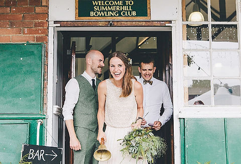 A smiling bride with flowers and two groomsmen at the door of the pavillion
